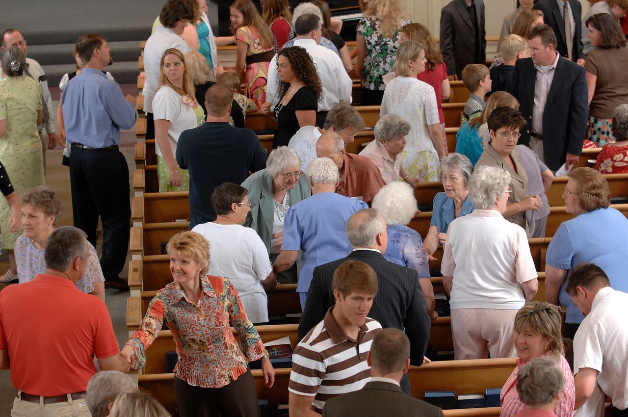 People exiting a church building, walking on stepped rows of pews, some smiling and talking.