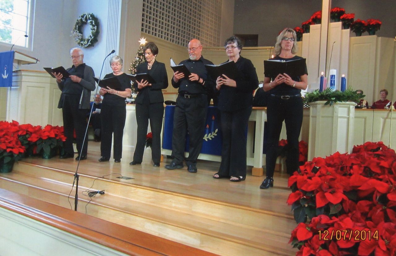 Choir singing on a church stage, surrounded by red poinsettias and Christmas decorations.