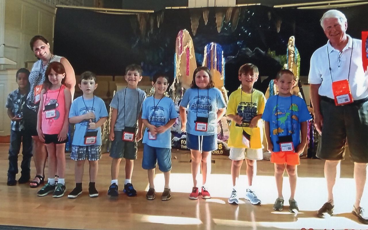 Group of children and adults posing onstage with colorful backdrop.