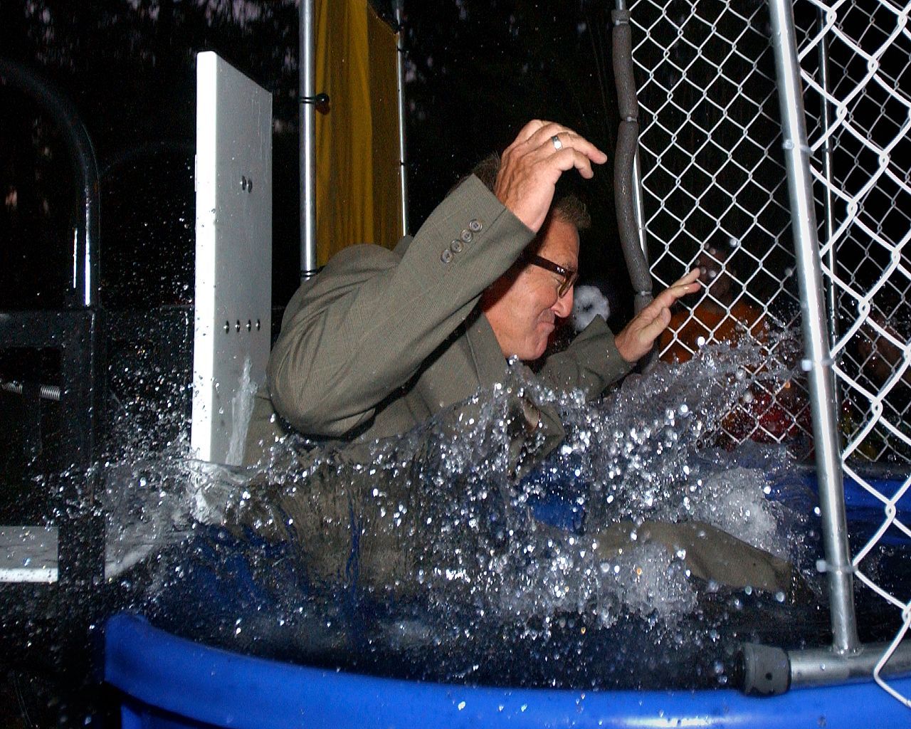 Man in suit falls into dunk tank, water splashing.
