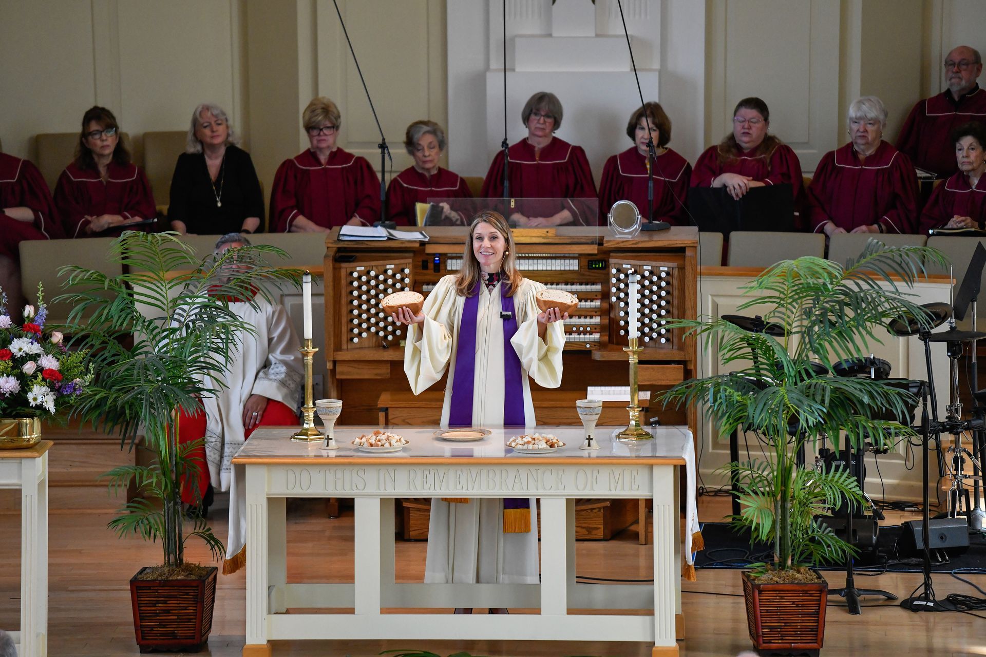 Woman in robe holding bread at a church altar, with a choir and organ in the background.