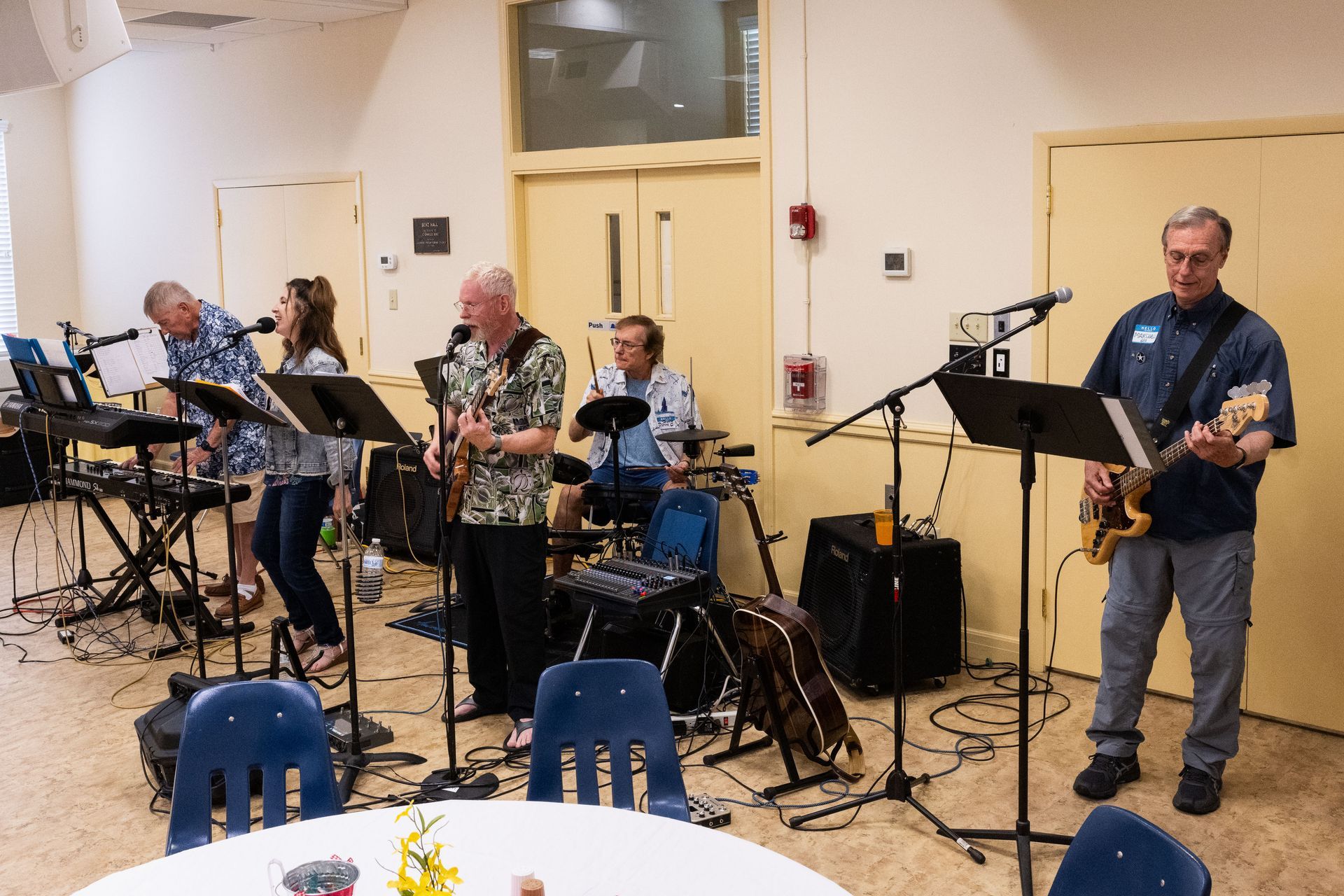 Band performing indoors: keyboards, guitar, drums, vocals. People playing instruments, microphone stands.