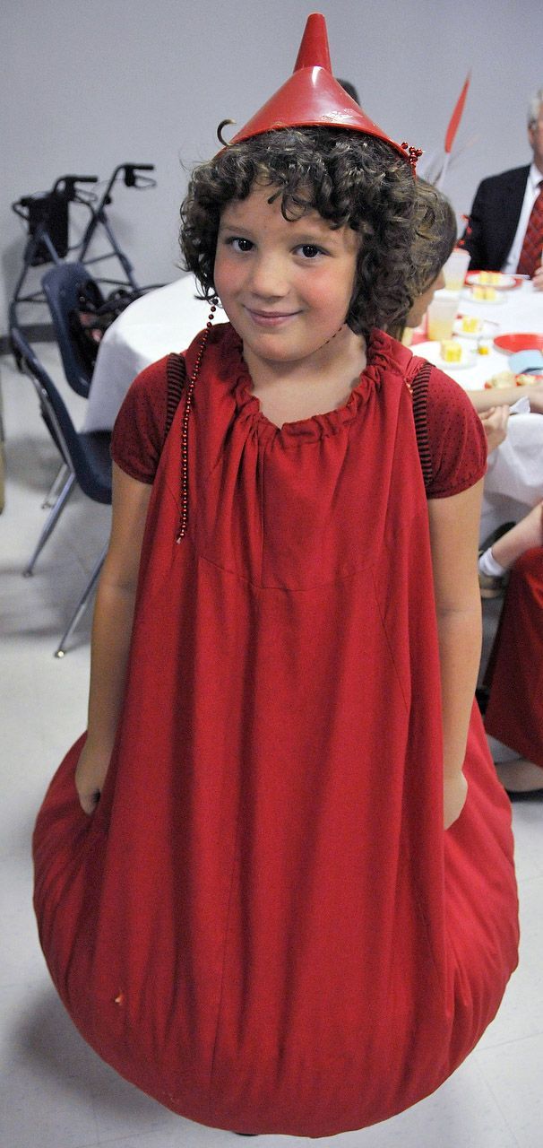 A child in a red costume and hat smiles at the camera, indoors.