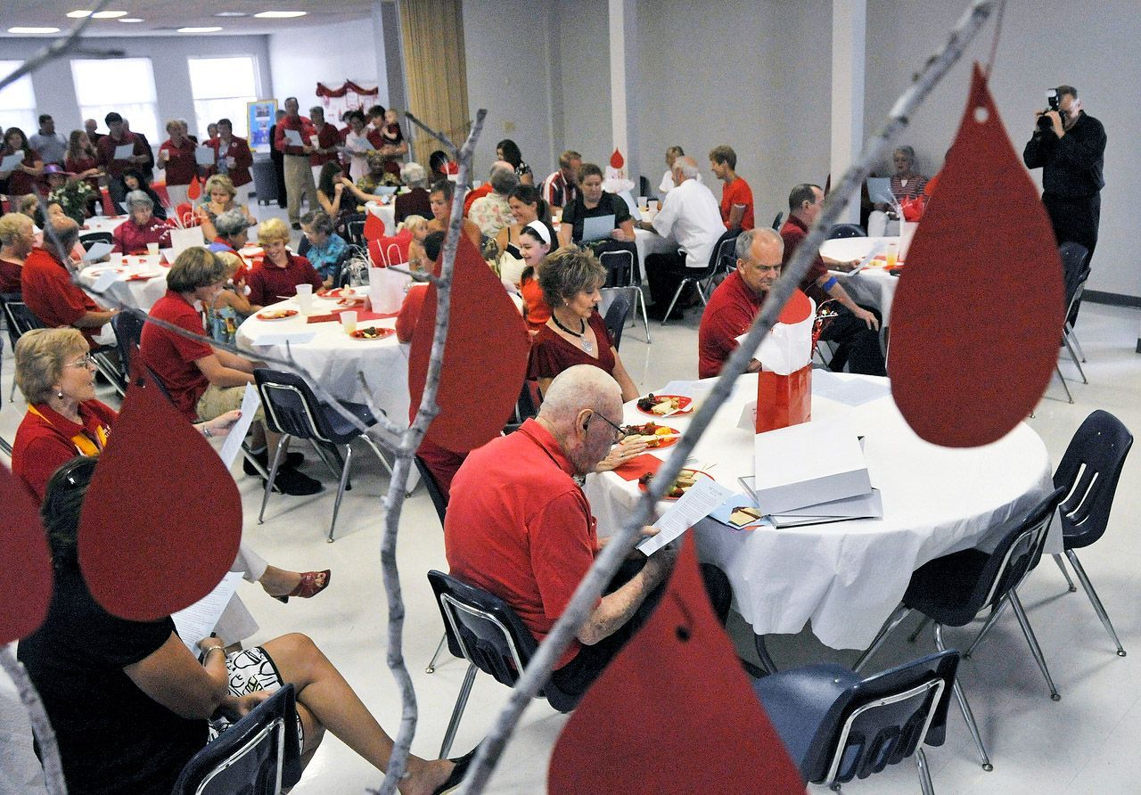 Event with people wearing red, gathered around tables. Red paper teardrops hang from branches.