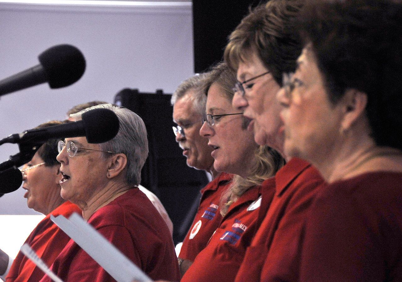 Choir singing with microphones, wearing red shirts.