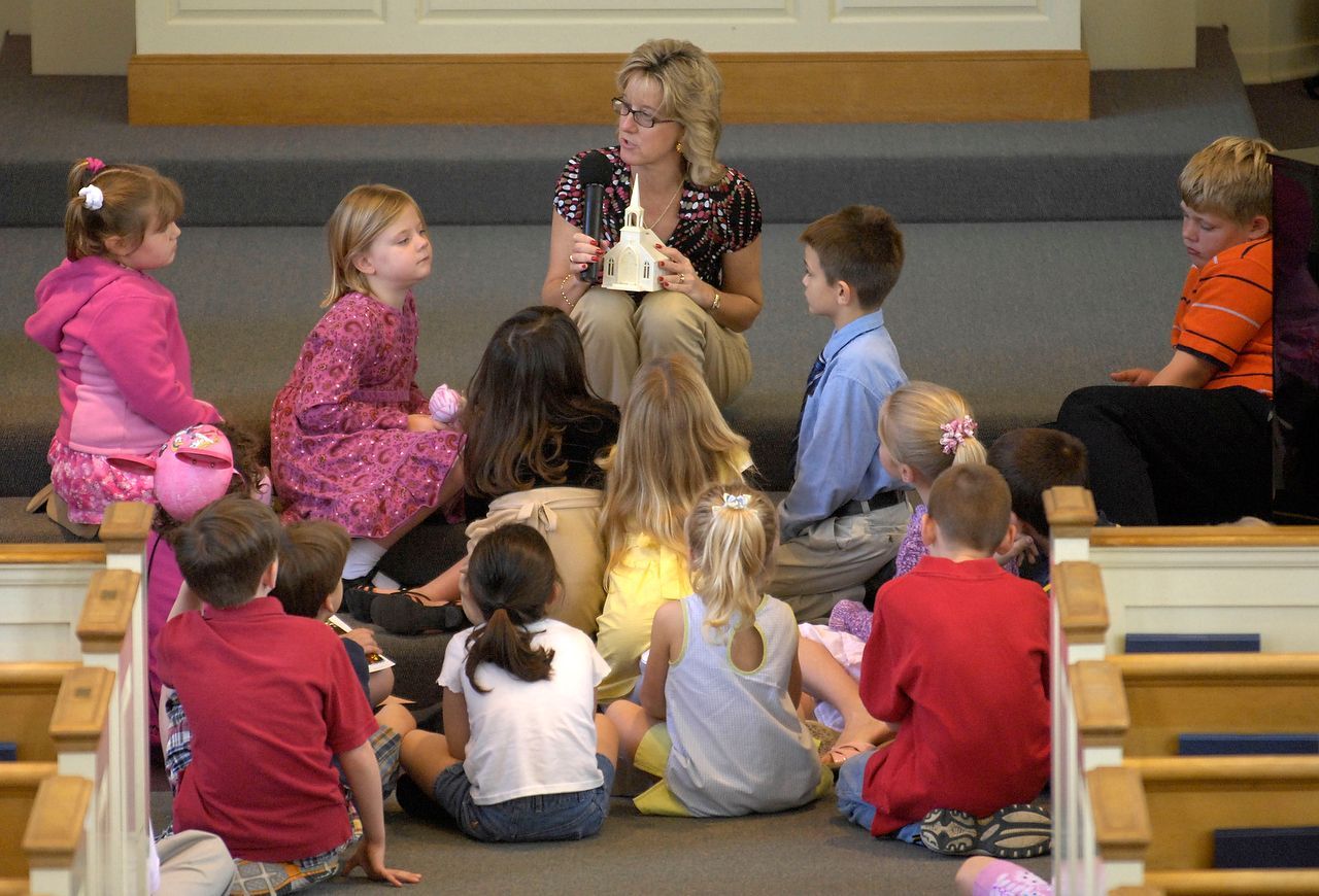 Teacher reading to group of children, seated on steps in a church.