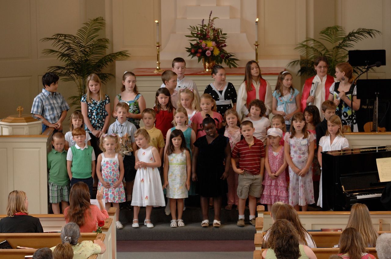 Children's choir singing on a stage in a church. Audience in pews.