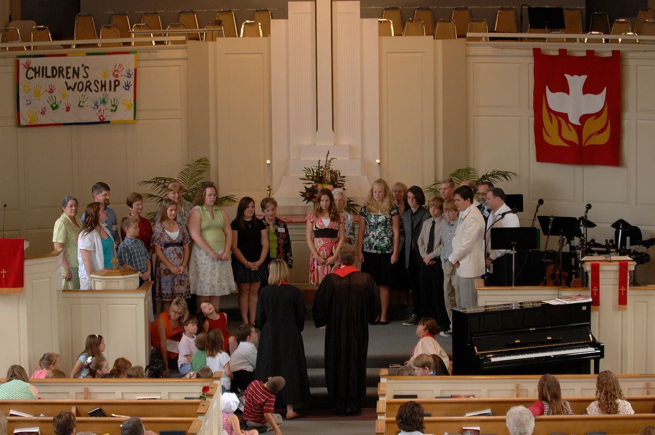Children and adults singing on a church stage, children's worship banner, red dove banner, piano.
