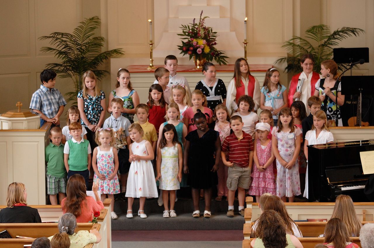 Children's choir performs on stage in a church, facing the audience.