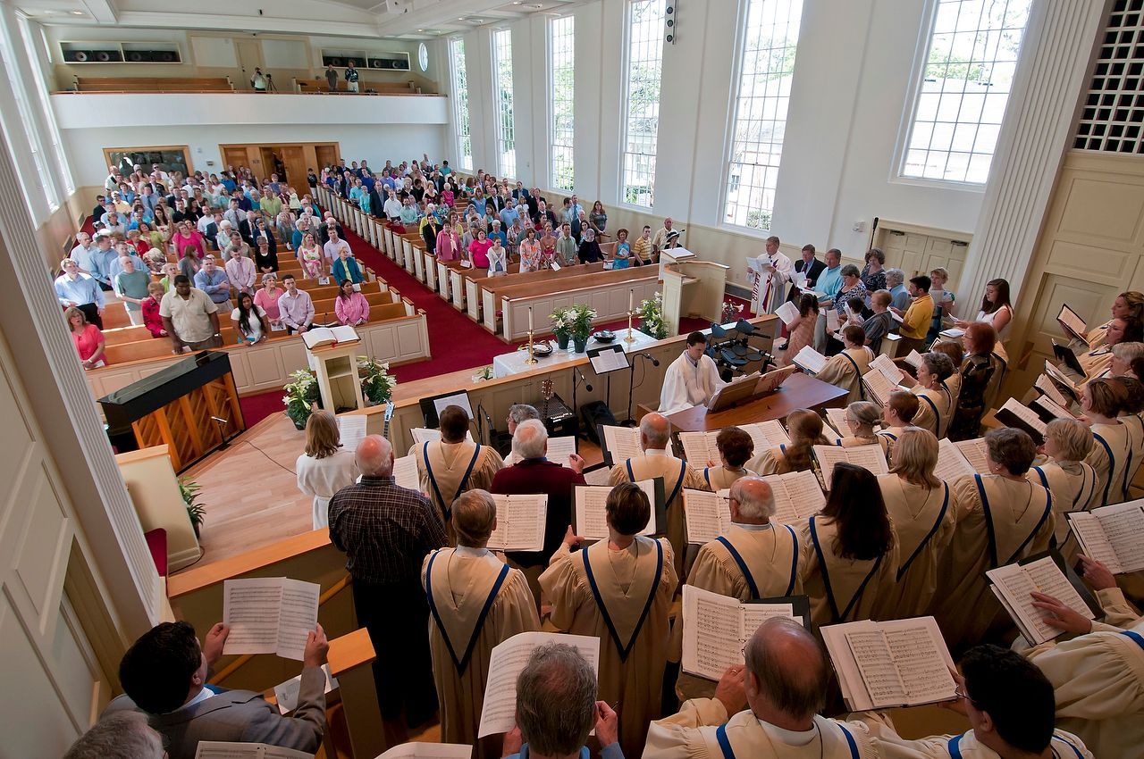 Church service with choir and congregation; people singing and listening in a light-filled sanctuary.