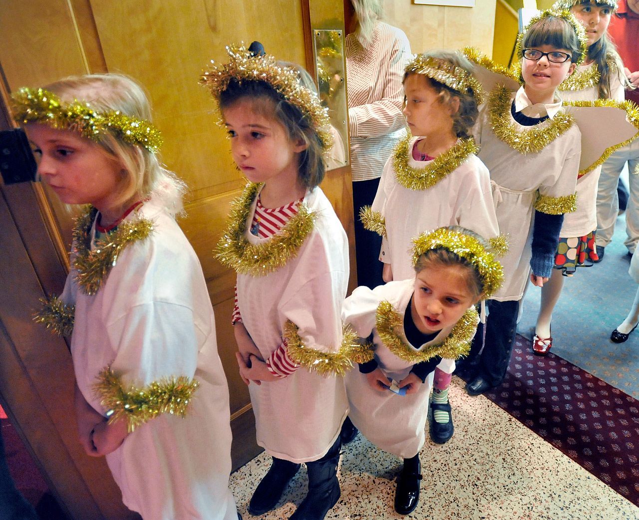 Children in white robes and gold halos lined up in a doorway.