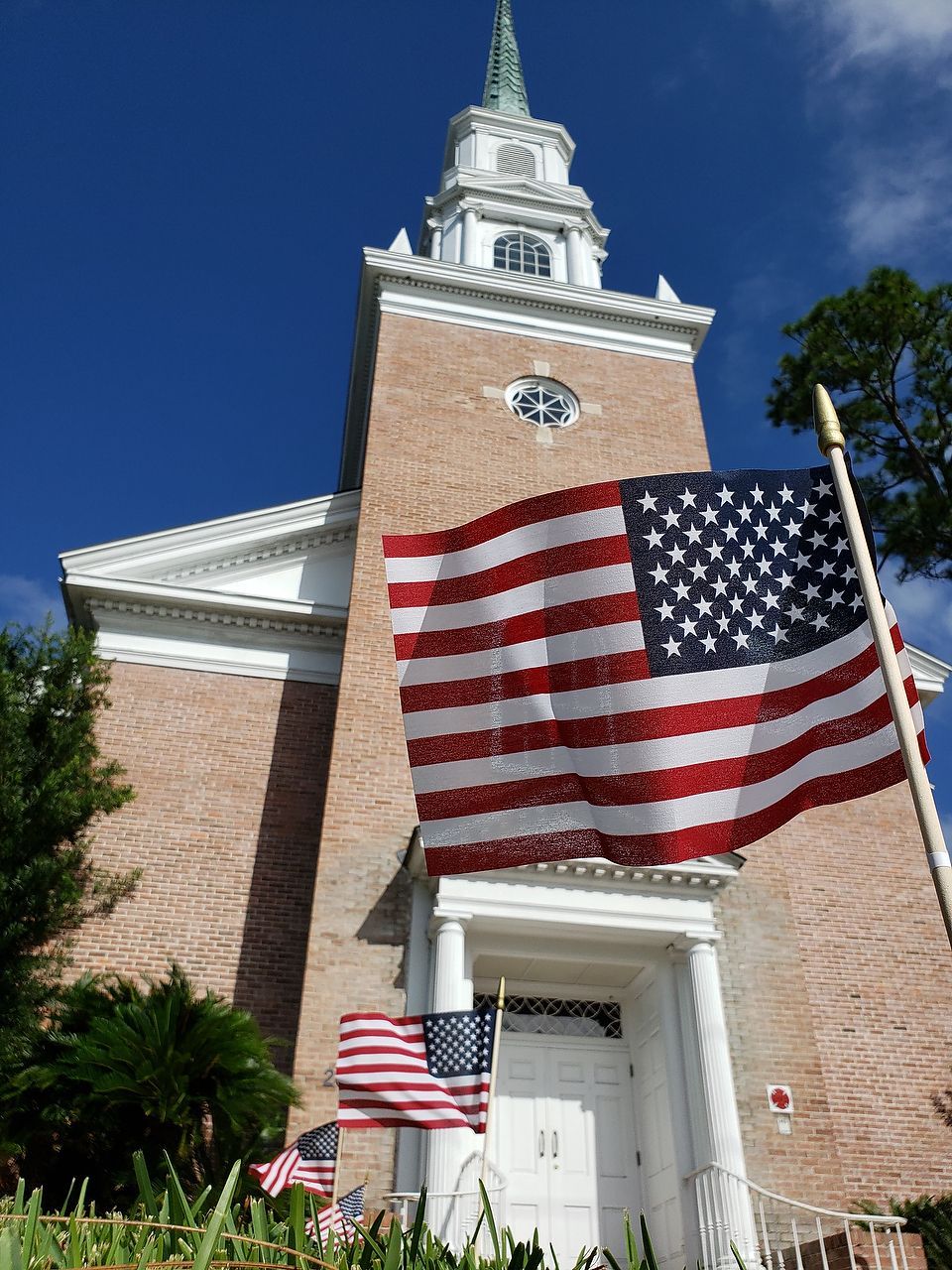 Brick church with steeple, waving American flags in front.