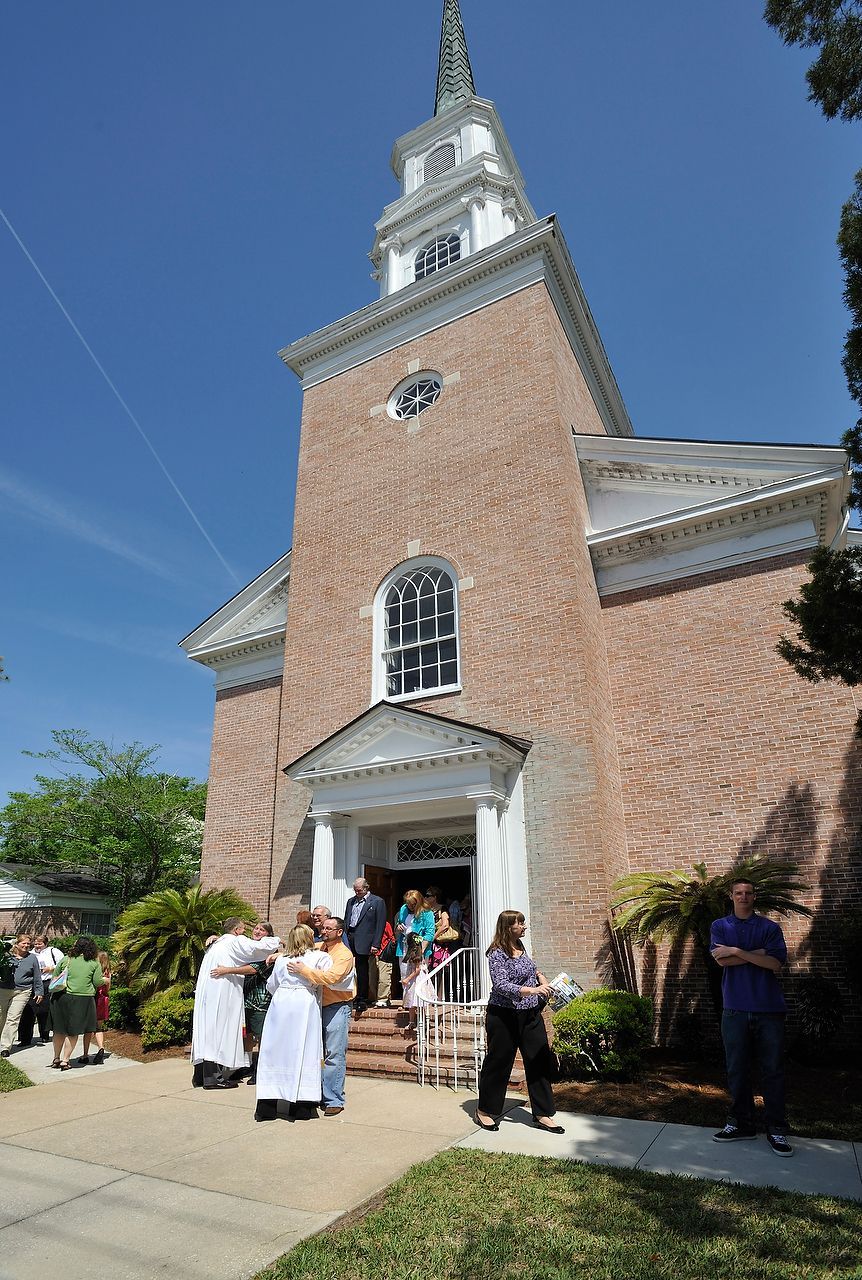 Brick church with a white steeple, people entering the front door on a sunny day.