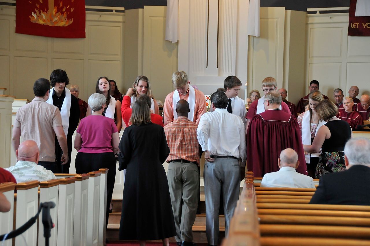 People in church, some wearing stoles, walk towards the altar. Others sit in pews.