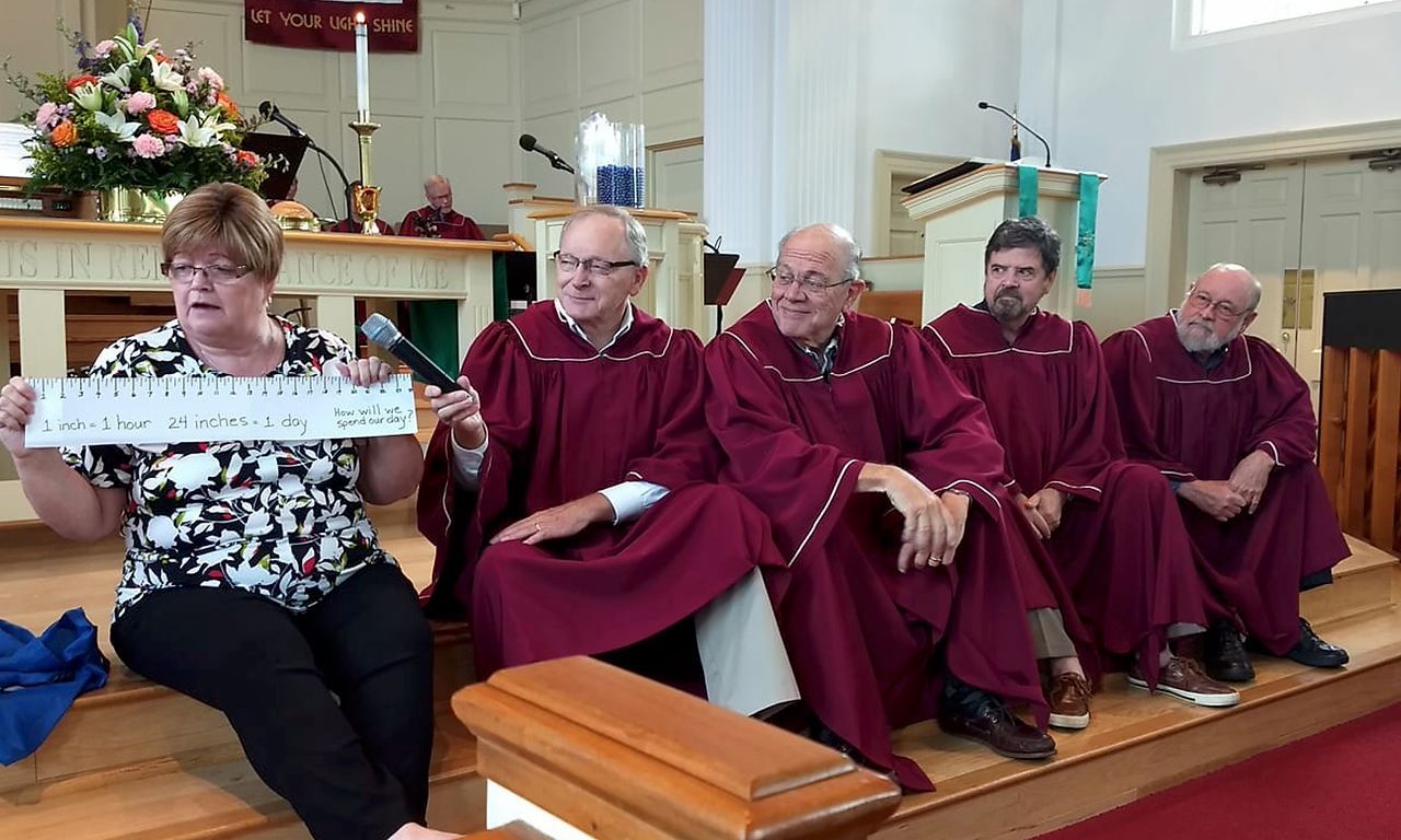 Woman holding sign with clergy in red robes seated on church steps.