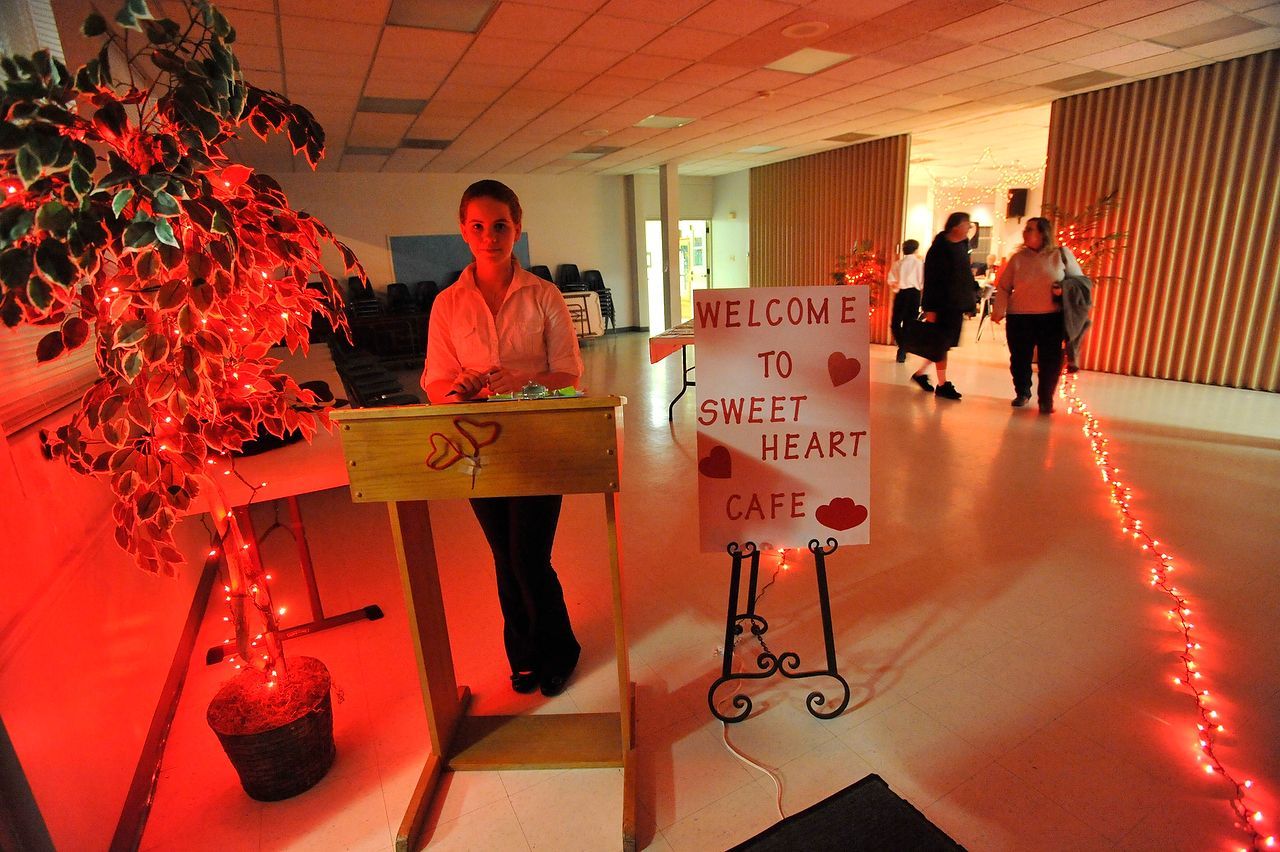 Person stands at a podium in a cafe entrance decorated for Valentine's Day. Sign says 
