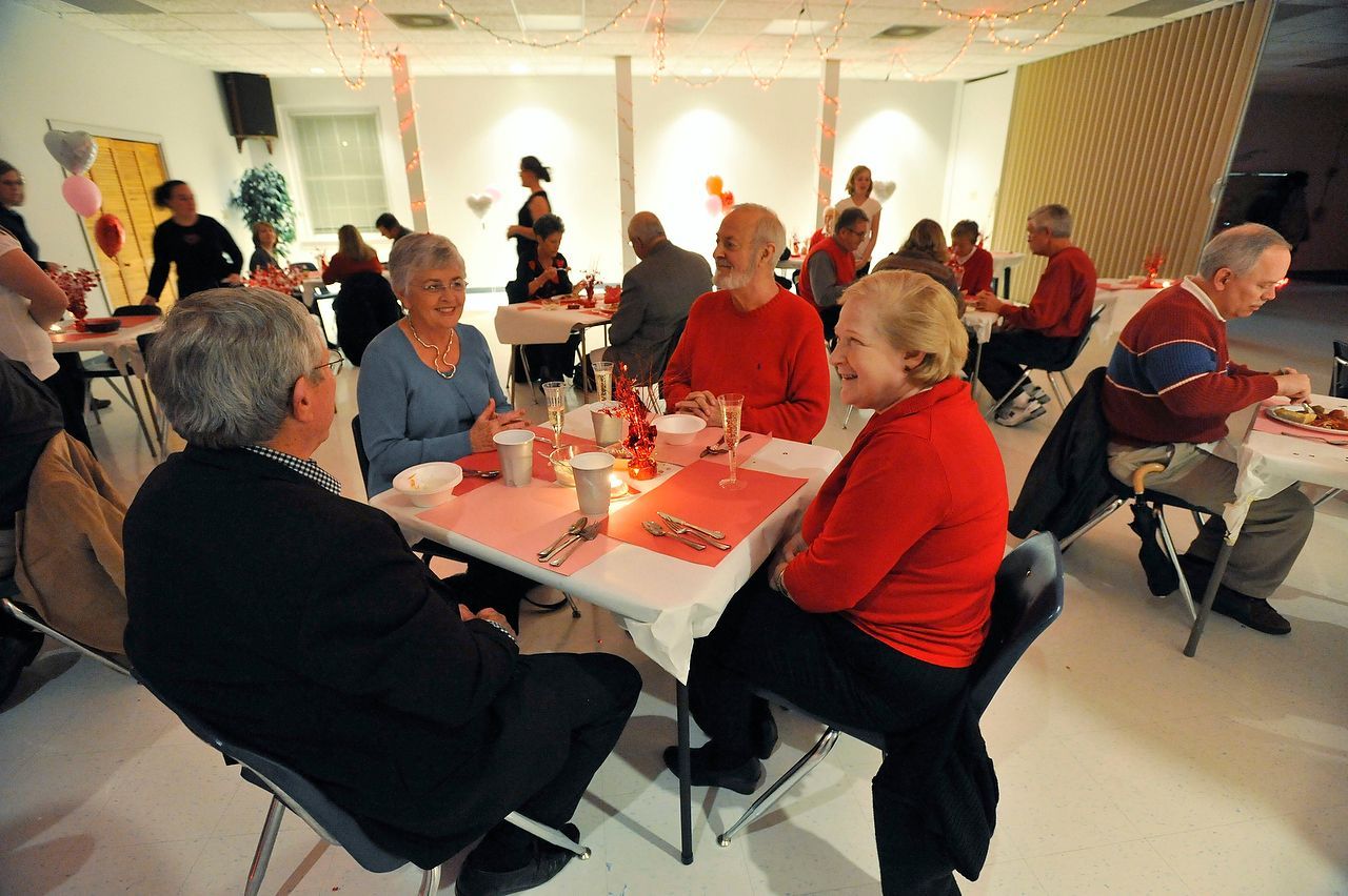 People gathered at tables in a brightly lit room, some wearing red.