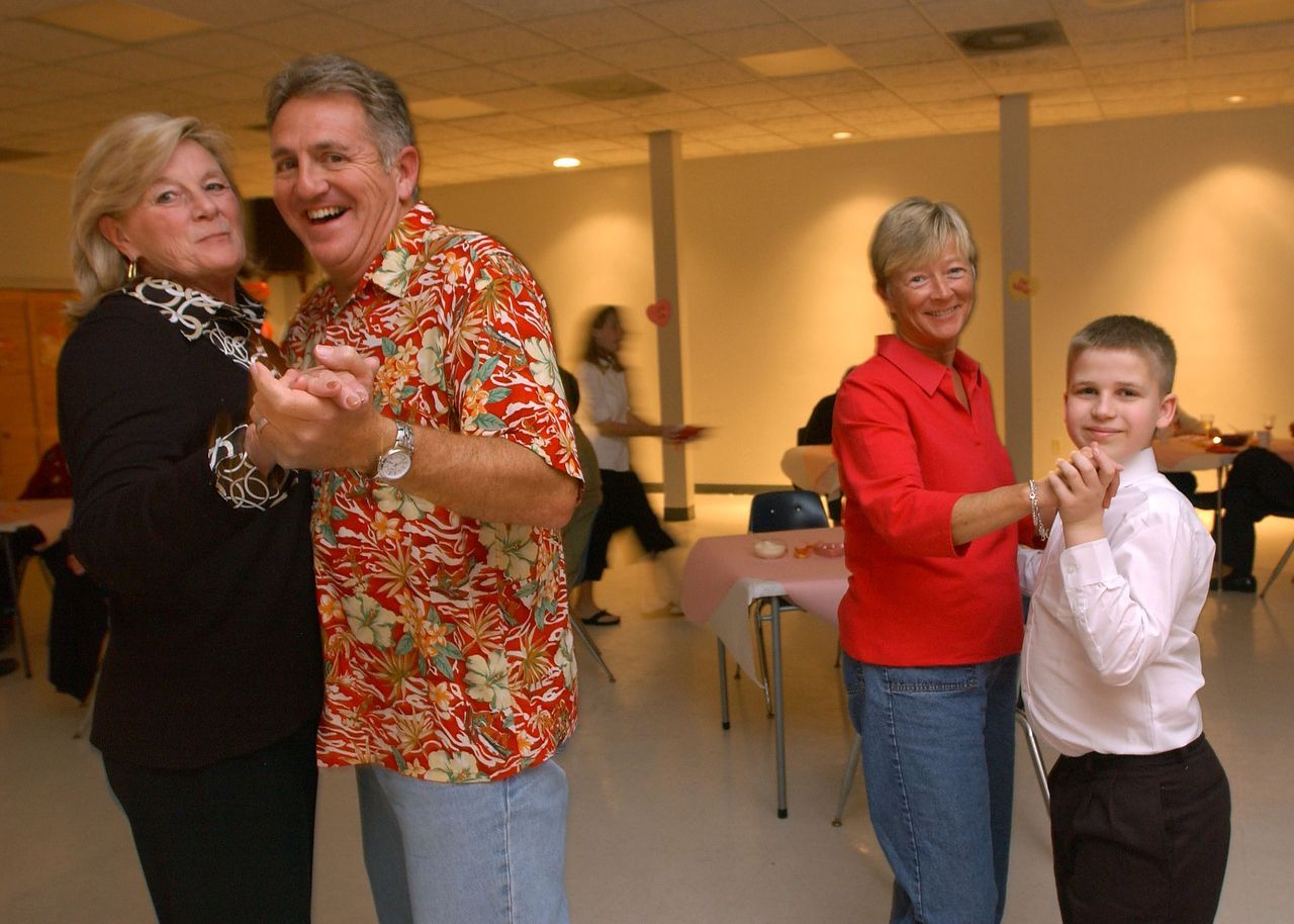 Two couples dancing in a brightly lit room. Smiling adults, one with a child.