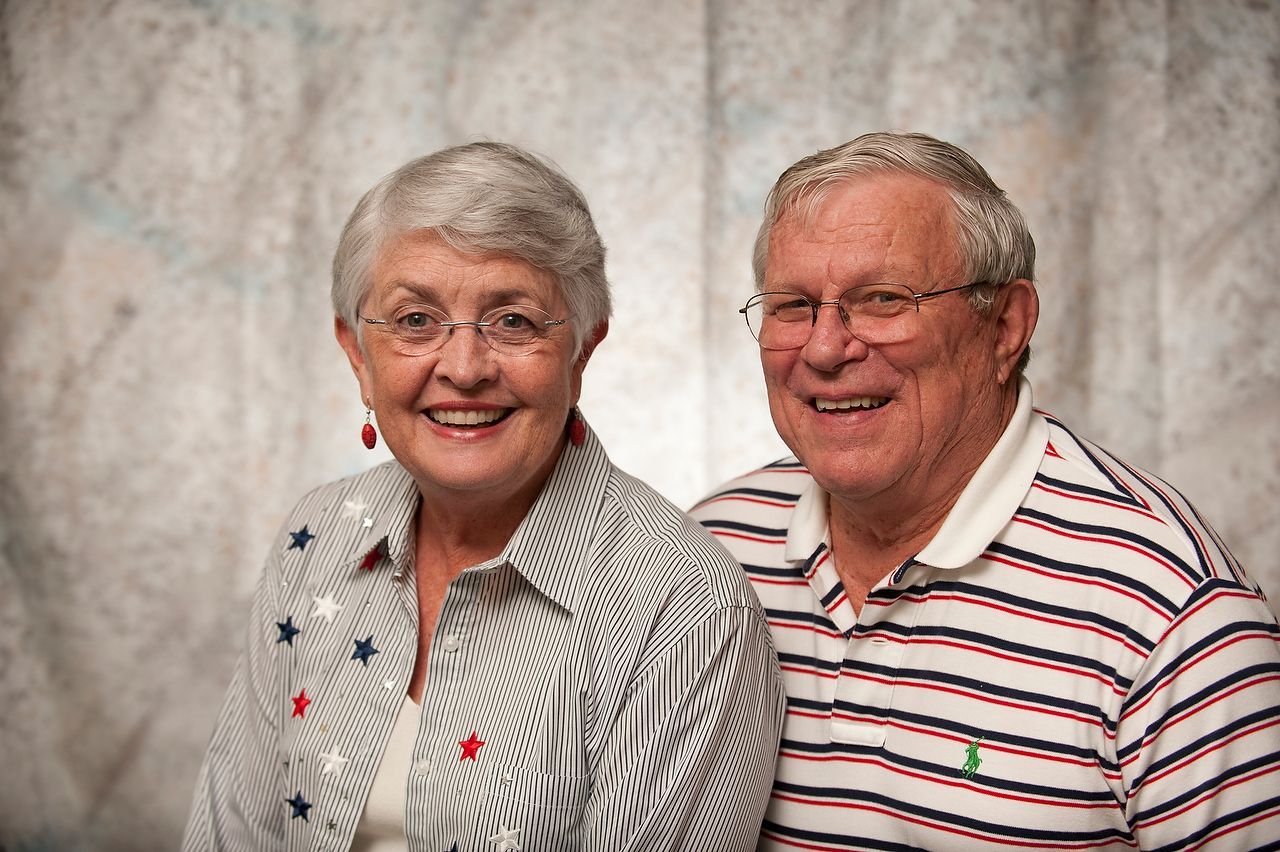 Smiling couple in glasses; woman in star-print shirt, man in striped polo.