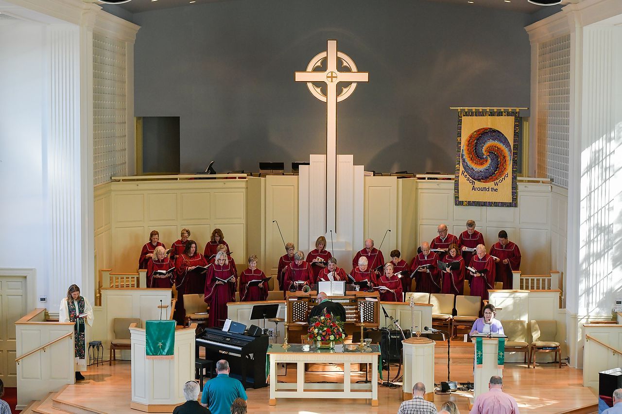 Choir in red robes performs in a church with a large cross above, colorful banner on the right.