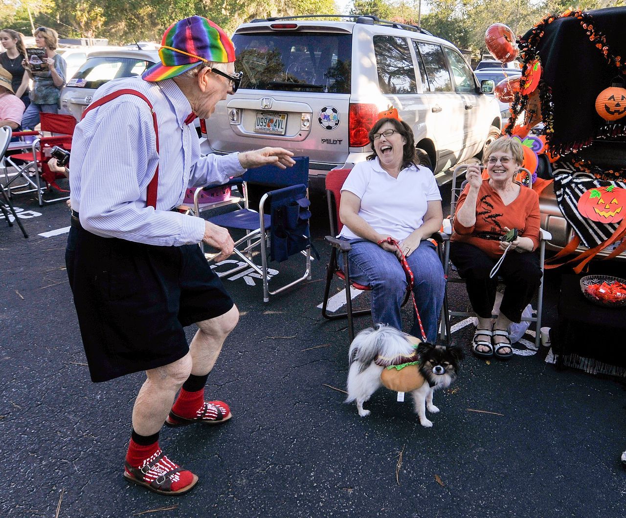 Man in costume dancing for two women and a dog at an outdoor event.