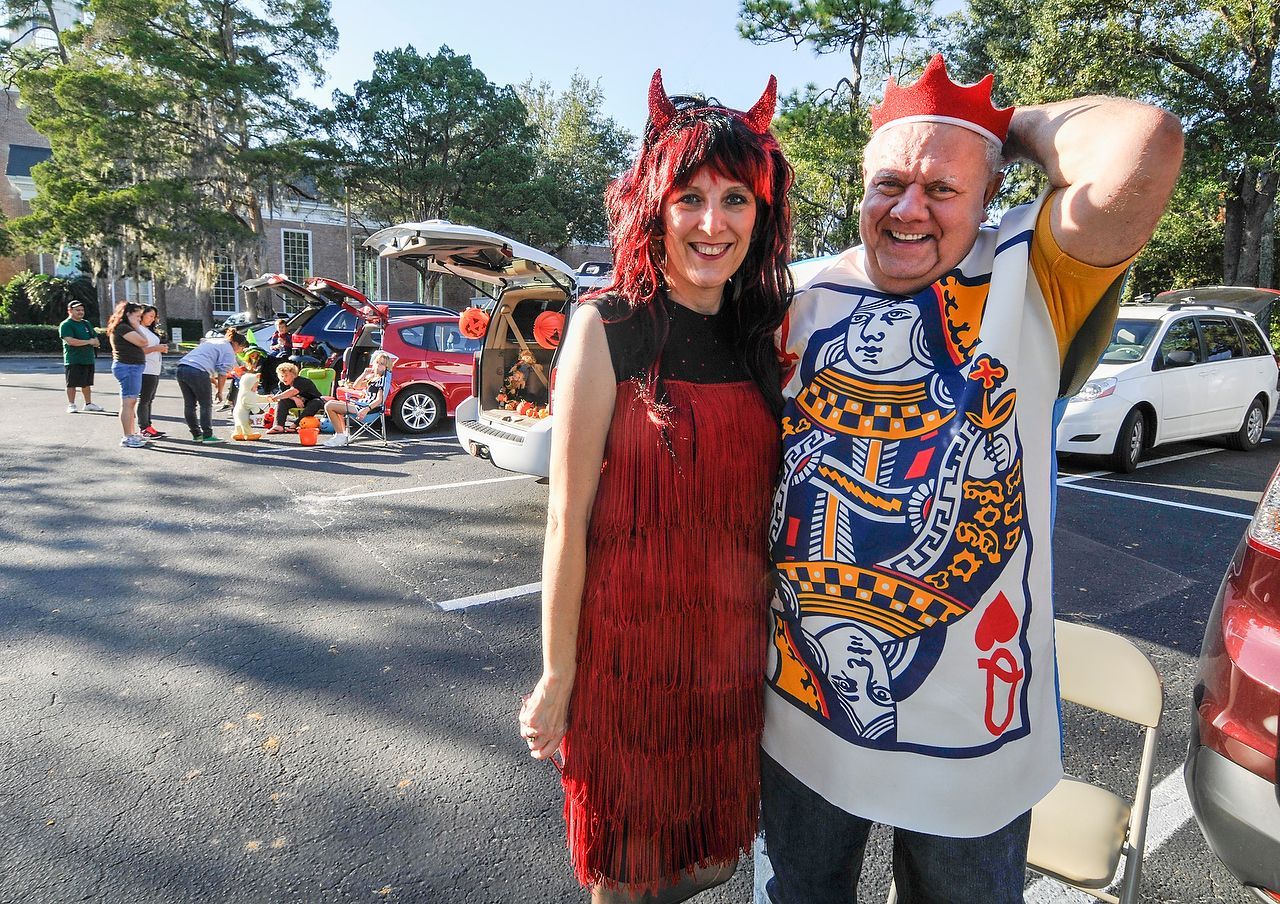 Couple in Halloween costumes posing at a trunk-or-treat event: red devil woman & King of Hearts man.
