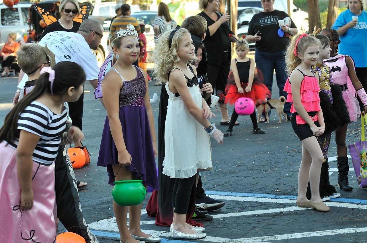 Children in Halloween costumes holding treat buckets in a parking lot, watching something.