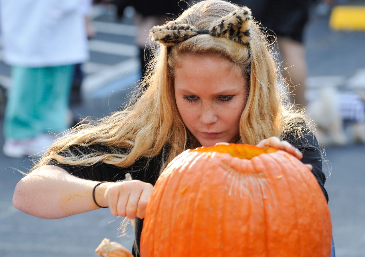 Woman carving a pumpkin, wearing a cat ear headband. Outdoor setting.
