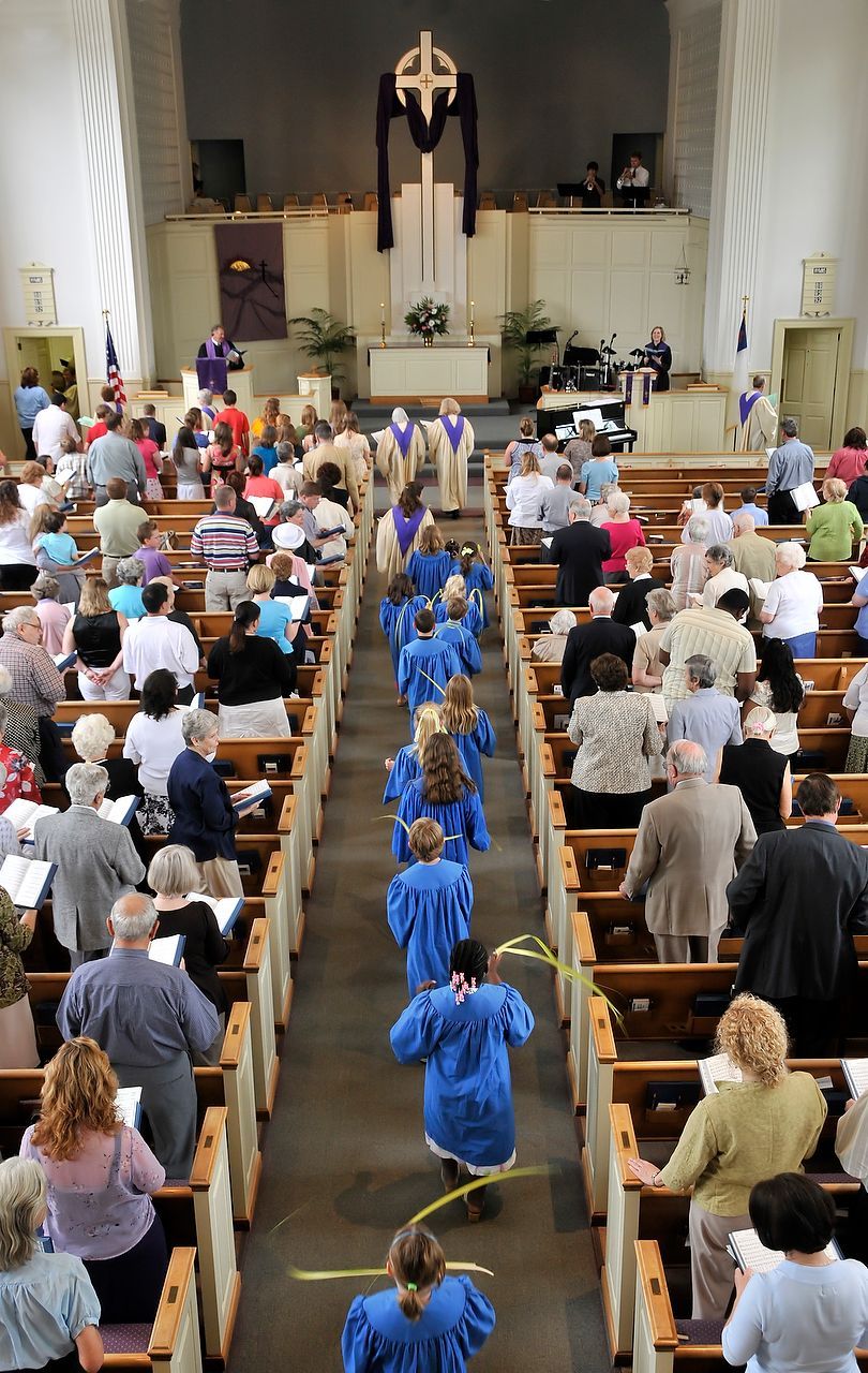 People in a church service. Procession of people in blue robes down the aisle, pews filled with seated congregants.