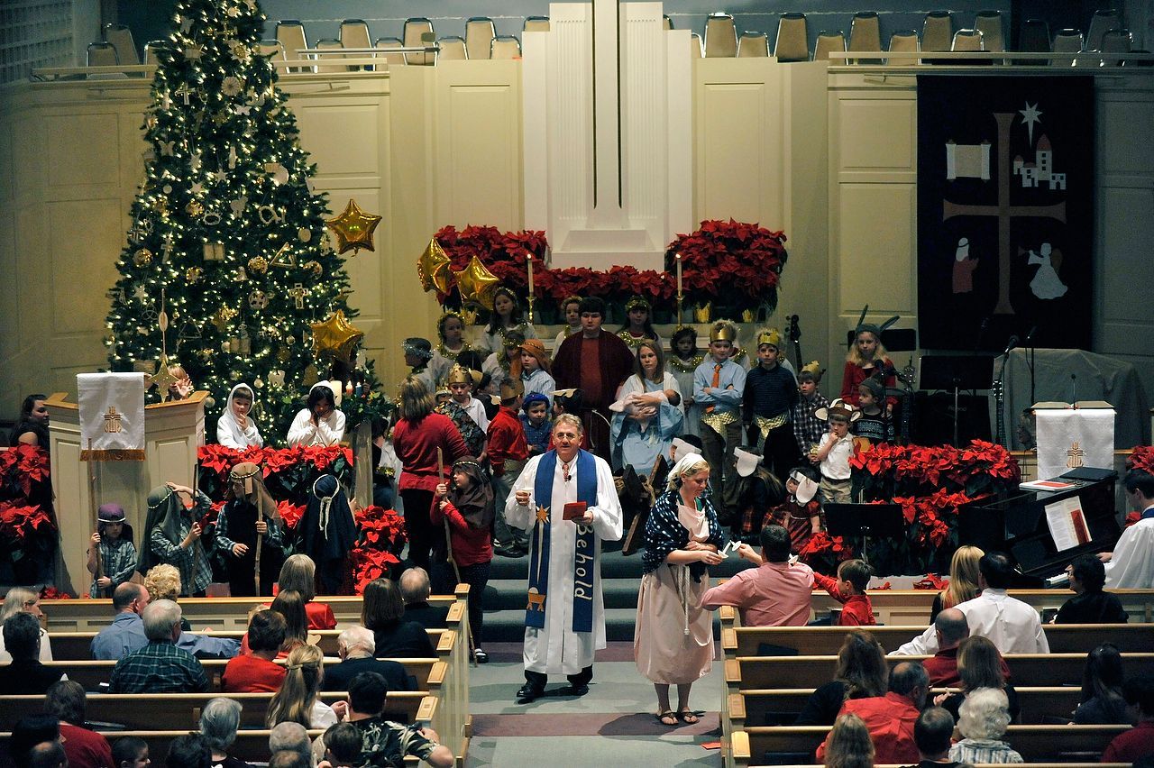 Church Christmas service with choir and tree, poinsettias, and pastor.