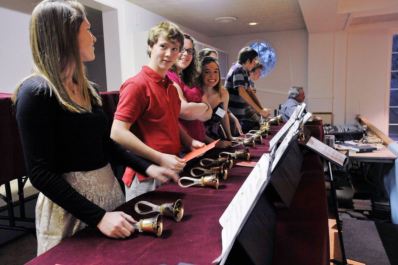 People playing handbells in a room; a few are smiling while looking at sheet music.