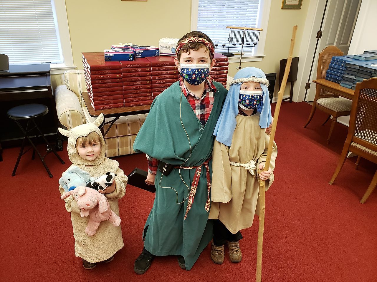 Children in costumes: sheep, shepherd, Mary, posing in a room with a red carpet.