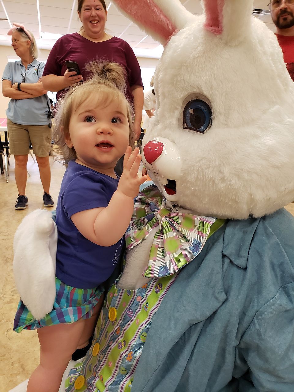 Child waving next to Easter Bunny costume. Indoor setting.