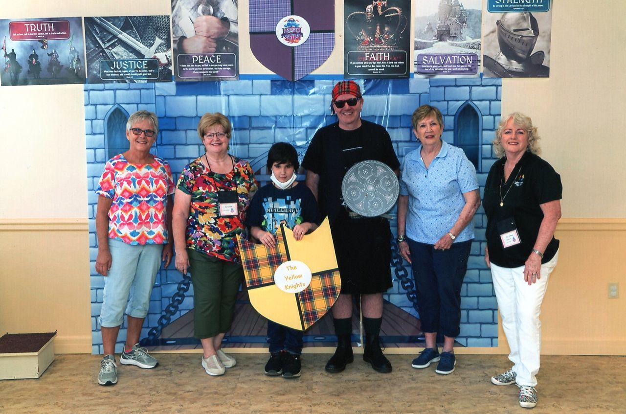 Group of six people posing in front of a blue castle backdrop, holding props.