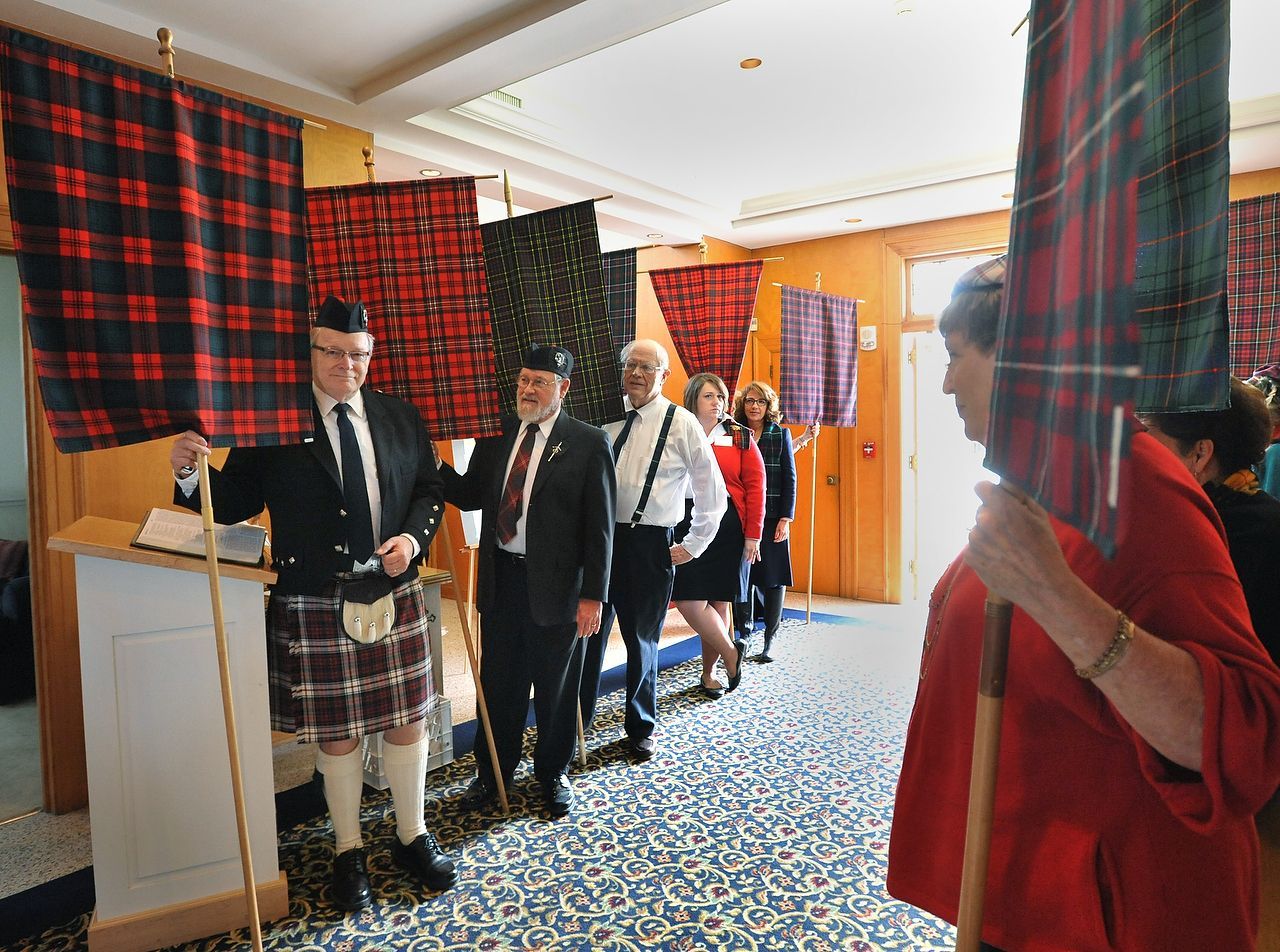 People in formal attire holding tartan banners, lining up indoors.