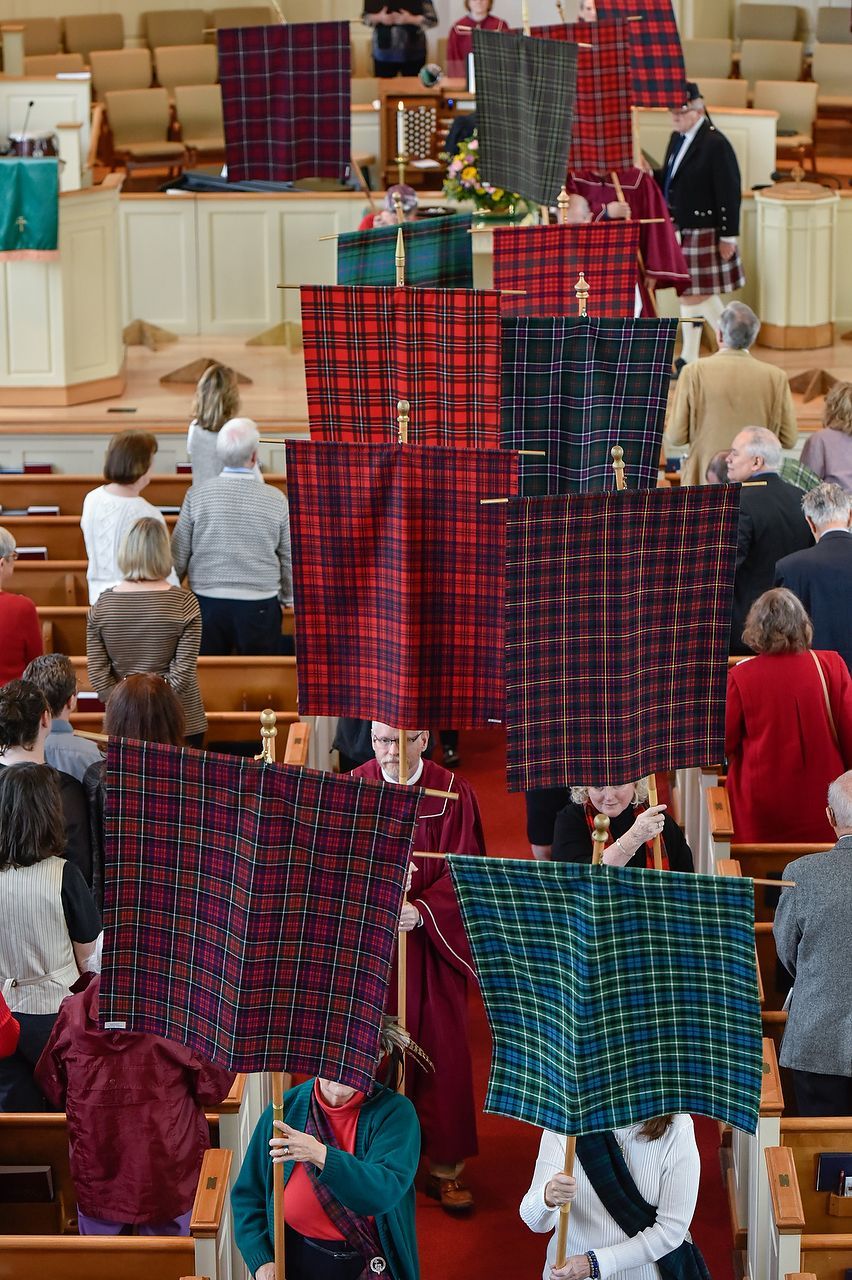 People in church procession carrying tartan banners.