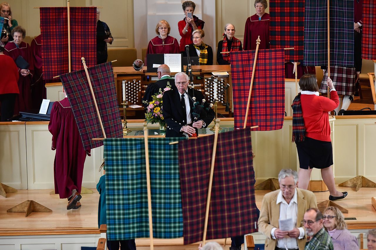 People in a church hold up tartan banners on stage. Some wear similar colors.