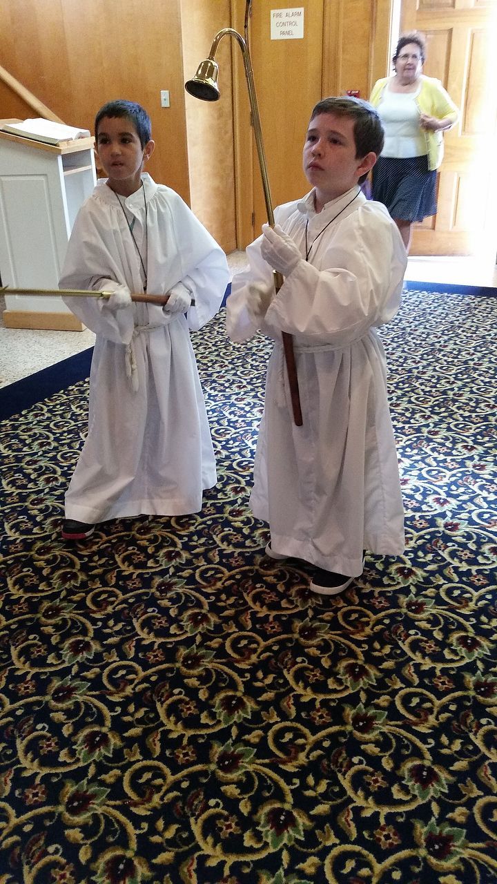 Two boys in white robes hold ceremonial items inside a building.
