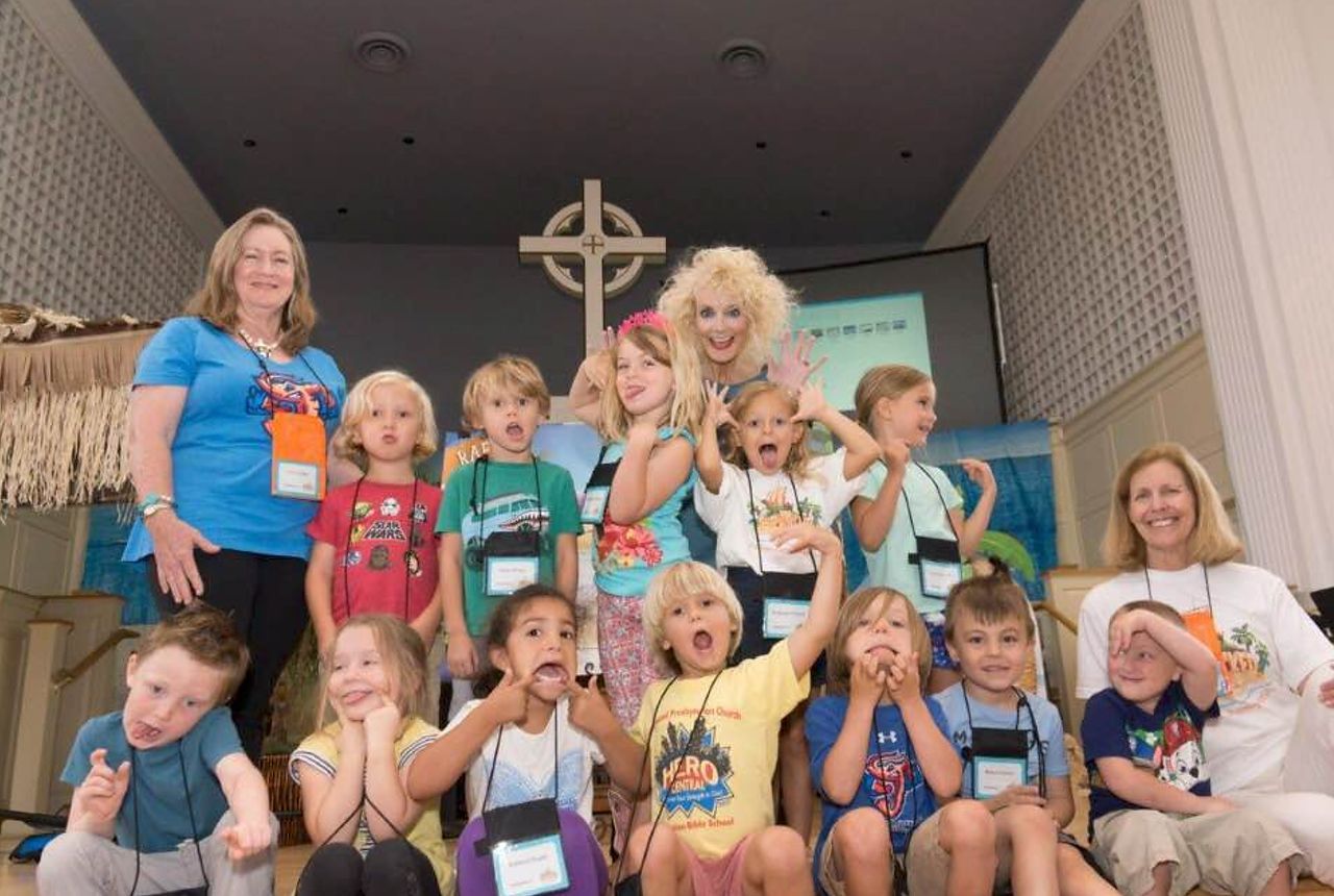 Children and adults pose in front of a cross; some make silly faces.