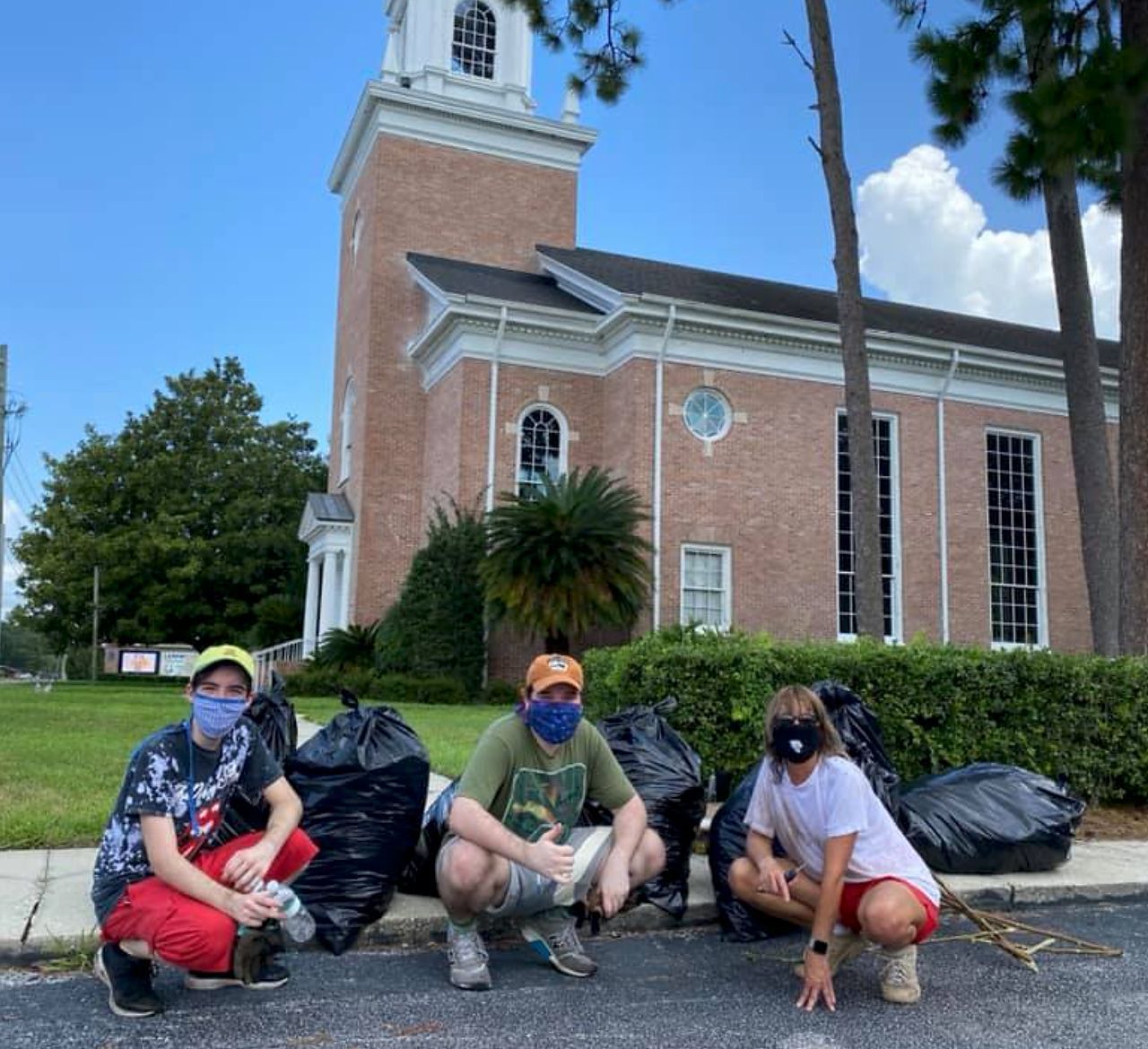 People squatting next to trash bags in front of a church. One is wearing a mask.