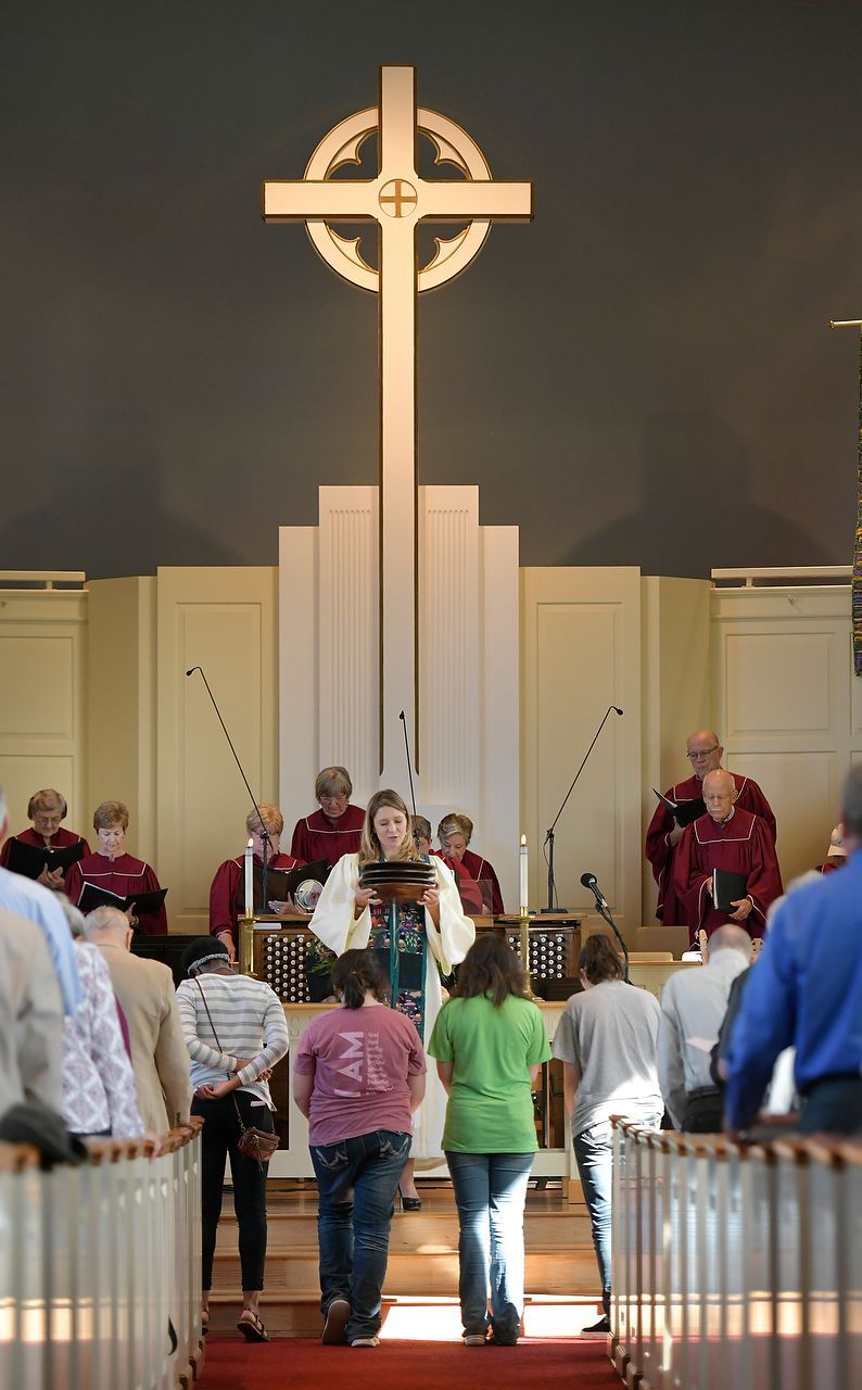 People in a church service with a cross above the podium, singing.