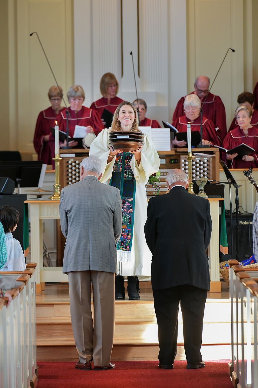 A woman in a white robe holds a platter, standing on a stage in a church.