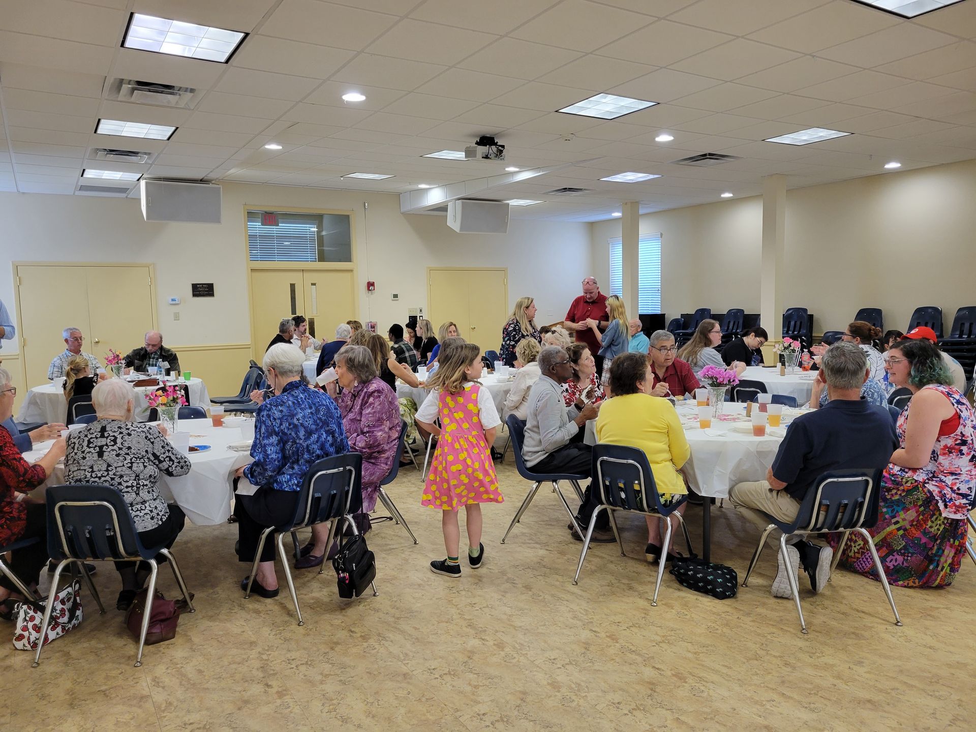 People seated at tables in a brightly lit room, likely a community gathering.