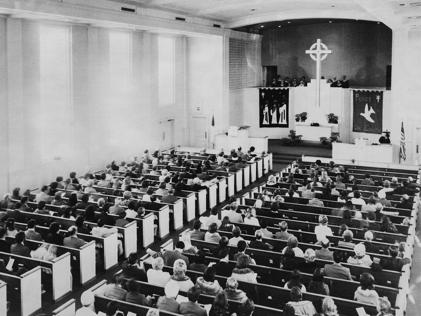 Large church interior with rows of people seated, facing a stage with a cross, banners, and a pulpit.