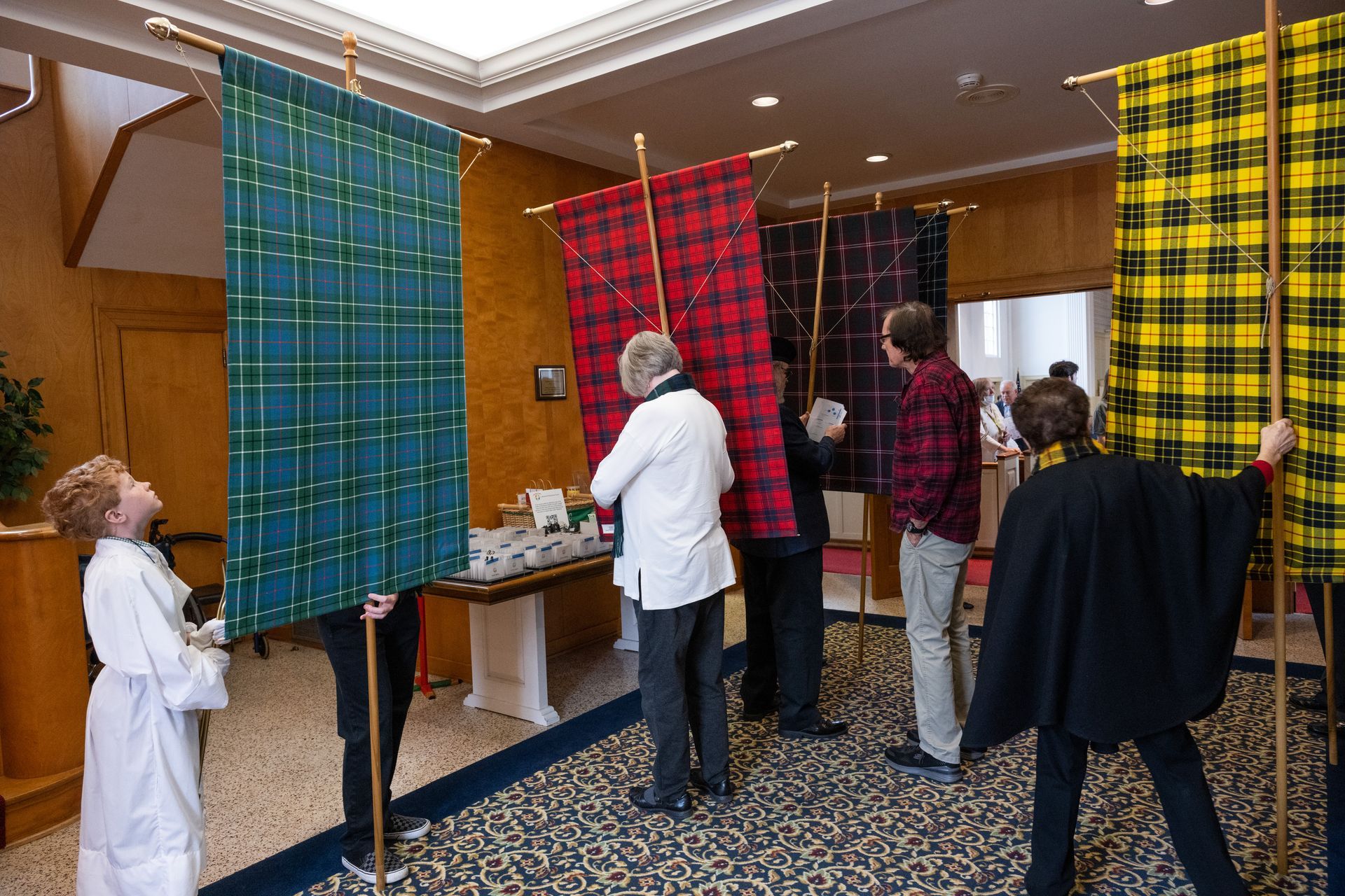 People holding and looking at large plaid banners in a room with a patterned carpet.