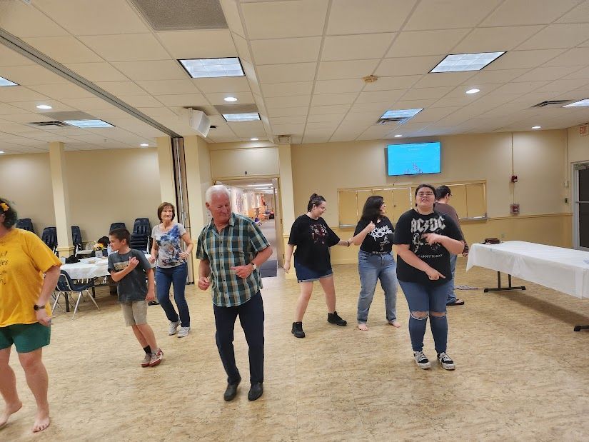 People dancing in a brightly lit room with a long table.