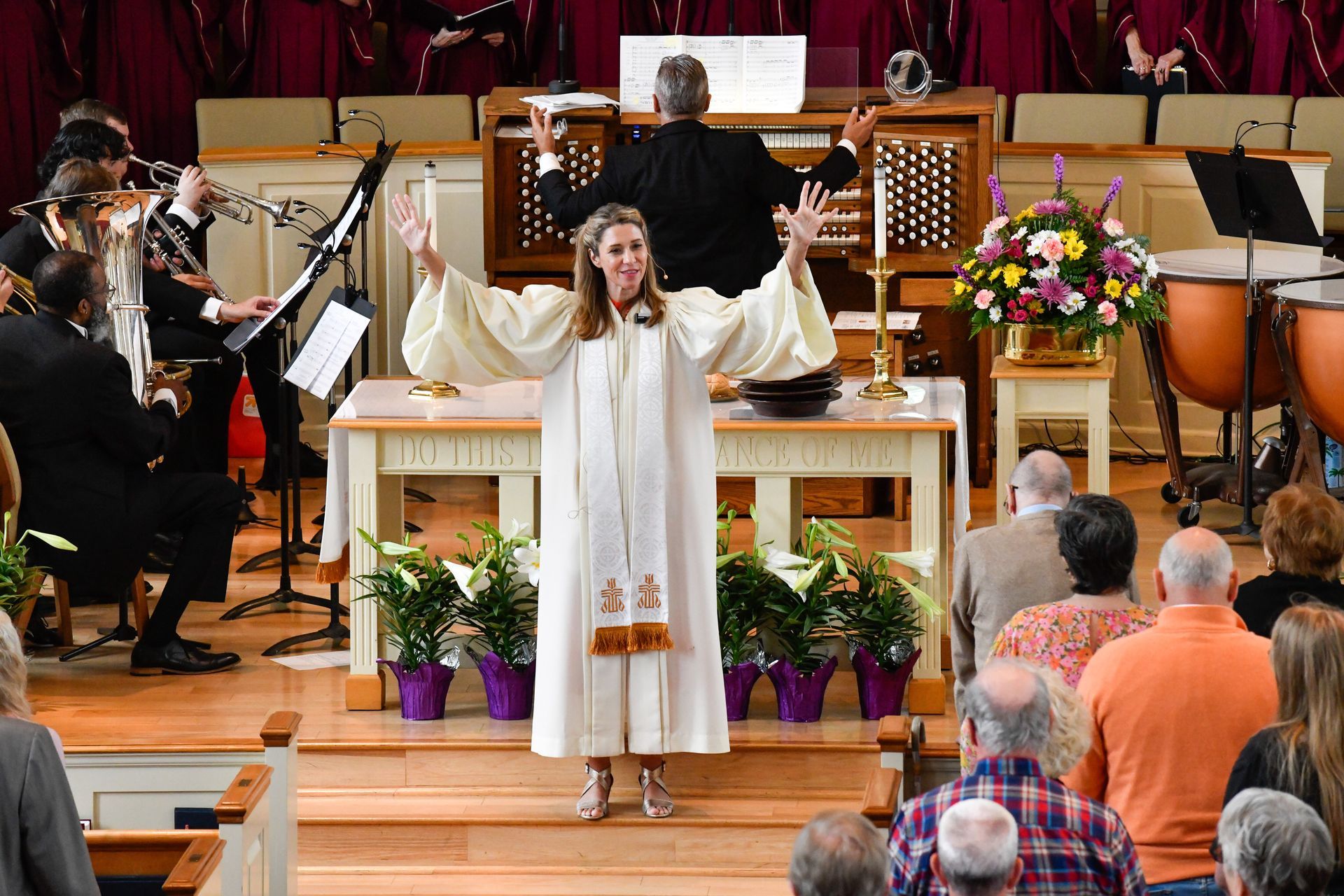 A woman in white robes leads a church service, arms raised. A choir, band, and congregation are visible.