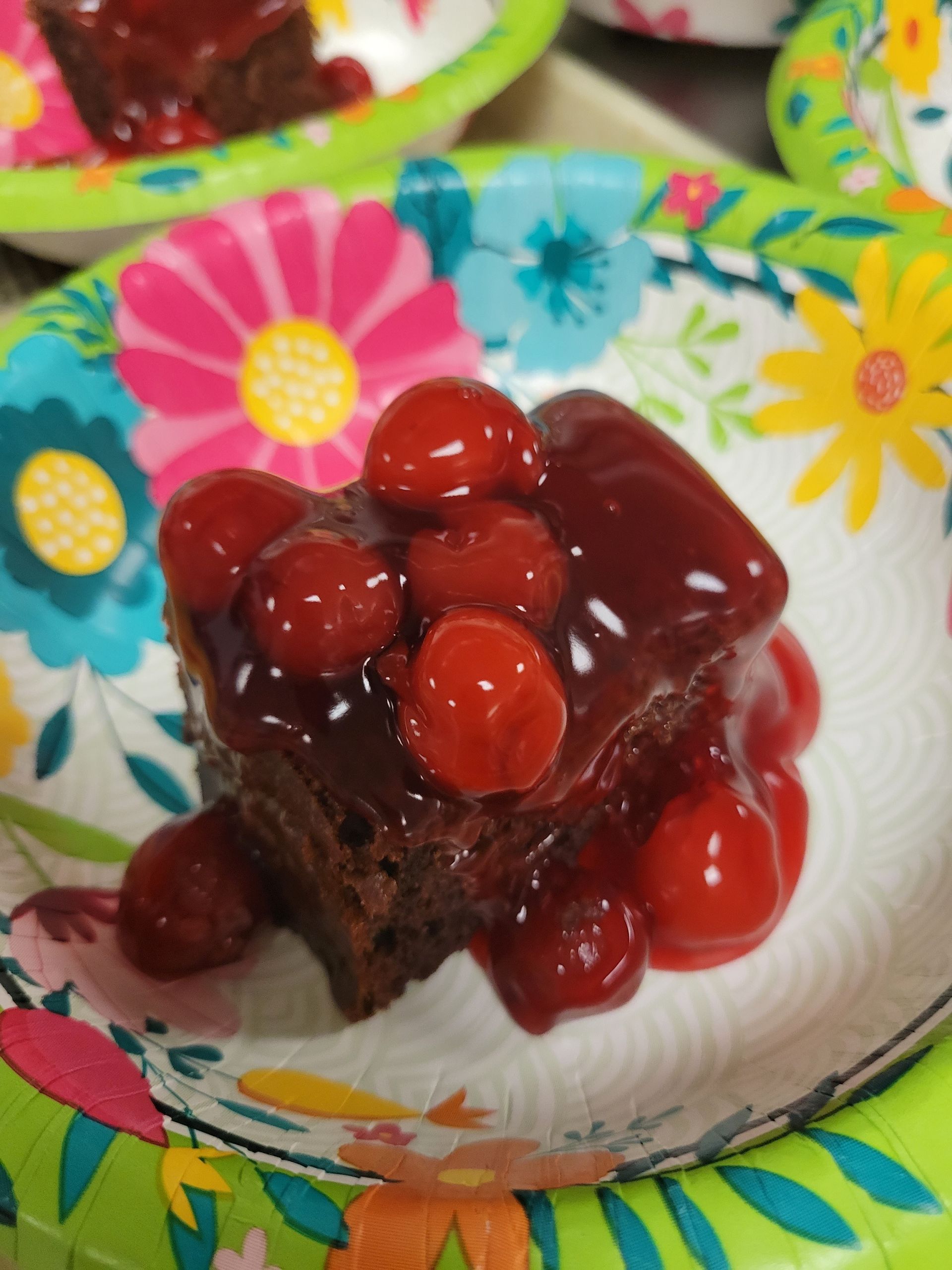Brownie topped with cherries and sauce on a floral paper plate.