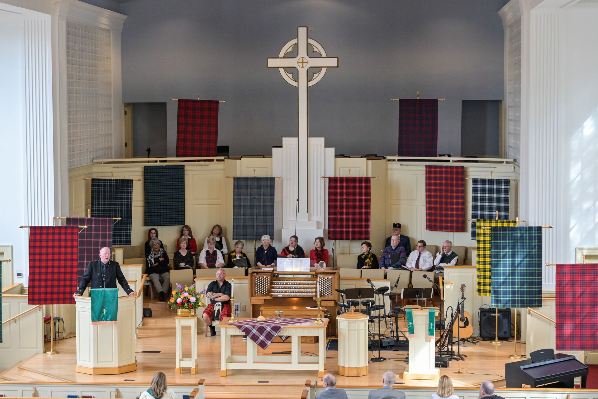 Church service with a speaker at the podium and a cross on the wall, decorated with tartan.