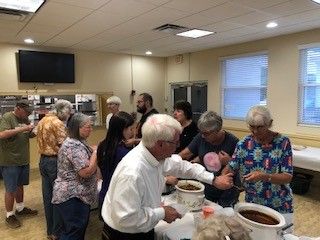 People at a gathering serving food from crockpots in a well-lit room.